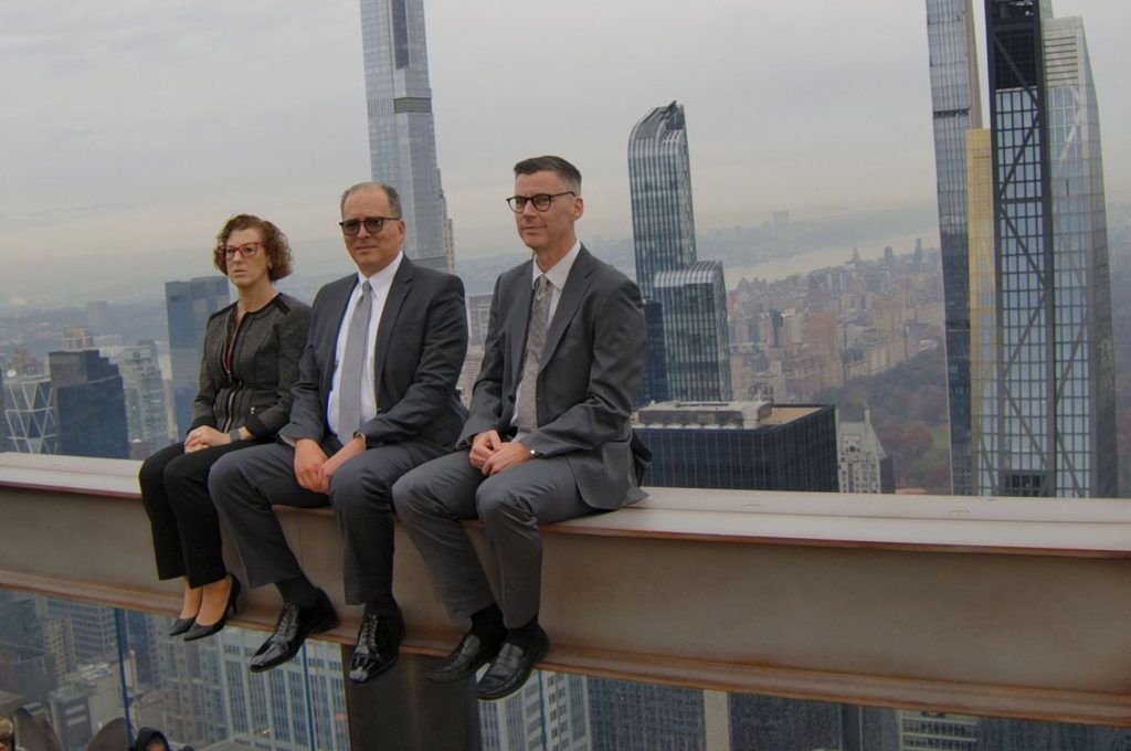 The Stonberg Hickman & Pavloff partners seated on a steel beam above Manhattan